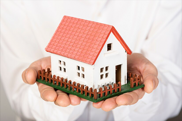 Man in white holding a model of a house in his hands.